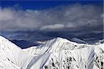 Snowy sunlit mountains and cloudy sky. Caucasus Mountains, Georgia, view from ski resort Gudauri.