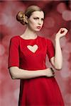 portrait of attractive blonde girl with cute hair-style and make-up posing with romantic style wearing red dress with sexy heart shaped neckline