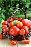 basket with different types of tomatoes on wooden table