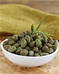 Pickled capers in white bowl on wooden table