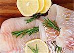 Arrangement of Raw Cod Fish Fillet with Lemon Slices and Rosemary closeup on Wooden background