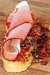 Delicious Spanish Tapas with Cured Ham Prosciutto, Slices of Paprika and Pepper on Toast with Olive Oil closeup on Wooden background