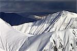 Snowy sunlit mountains and overcast sky. Caucasus Mountains, Georgia, view from ski resort Gudauri.