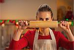 Young housewife holding rolling pin in front of face