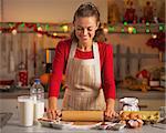 Happy young housewife rolling pin dough in christmas decorated kitchen