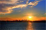 The sun setting over beautiful Sydney Harbour, its golden orange rays bouncing off the underside of the clouds, and that's  Sydney City in distance as a silhouette.  Ahh summer in the city.