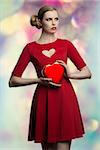 portrait of romantic blonde woman with creative hair-style and red sexy dress taking in the hands one  box of chocolates