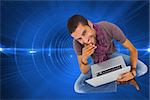 Composite image of thoughtful man sitting on floor using laptop and smiling at camera