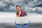 Composite image of thinking man sitting on floor using laptop and smiling