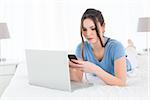 Relaxed young woman text messaging while using laptop in bed at home