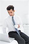 Serious young businessman with coffee cup using laptop at a hotel room