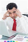 Portrait of a serious young businessman with laptop and graphs sitting at office desk