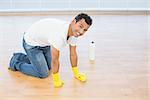 Side view portrait a smiling young man cleaning the parquet floor at house