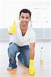 Portrait of a smiling young man cleaning the floor while gesturing okay sign at house