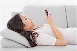 Side view of a relaxed young woman text messaging on sofa in living room at home