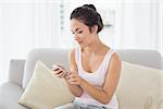 Relaxed young woman text messaging on sofa in living room at home