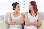 Unhappy young female friends not talking after argument at home on the couch