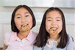 Portrait of two smiling young girls enjoying cookies in the kitchen