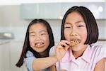 Little girl feeding her elder sister a cookies in the kitchen at home