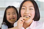 Close-up of a little girl feeding her elder sister a cookies in the kitchen at home