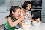 Two happy young girls eating cereals in the kitchen at home