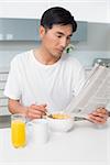 Serious young man having cereals while reading newspaper in the kitchen at home