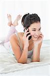 Beautiful smiling young woman using mobile phone in bed at home