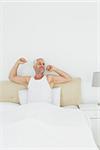 Mature smiling man stretching his arms in bed at home