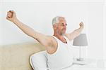 Mature smiling man stretching his arms in bed at home