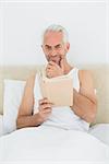 Portrait of a relaxed mature man reading book in bed at house