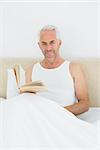 Portrait of a relaxed mature man reading book in bed at house
