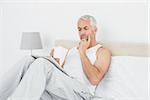 Mature man with coffee cup reading newspaper in bed at home