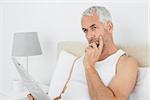 Casual thoughtful mature man with newspaper in bed at home