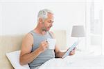 Side view of a mature man with digital tablet and coffee table sitting in bed at home