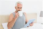 Mature man with digital tablet drinking coffee in bed at home