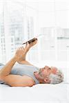 Side view of a relaxed mature man using digital tablet in bed at home