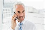 Close-up of a smiling mature businessman using mobile phone in a bright office