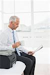 Side view of a mature businessman with coffee cup reading newspaper by luggage at a hotel room