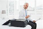Side view portrait of a mature businessman with coffee cup reading newspaper by luggage at a hotel room