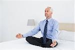 Full length of a relaxed mature businessman sitting in lotus posture on bed at home