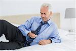 Smiling relaxed well dressed man text messaging in bed at home