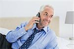 Smiling relaxed well dressed man using mobile phone in bed at home