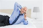 Relaxed mature businessman using mobile phone in bed at home