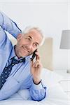 Close-up of a relaxed mature businessman using mobile phone in bed at home