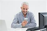 Smiling mature businessman with cellphone, laptop and computer at desk against white background
