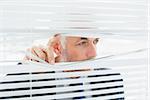 Close-up of a serious mature businessman peeking through blinds in the office
