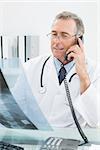 Male doctor looking at x-ray picture while using the telephone at medical office