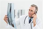 Male doctor looking at x-ray picture while using the telephone at medical office