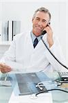 Portrait of a smiling male doctor using telephone at the medical office