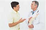 Male doctor showing patient something on skeleton model over white background